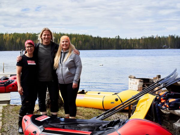 Kaksi naista ja mies järven rannalla kumilauttojen kanssa