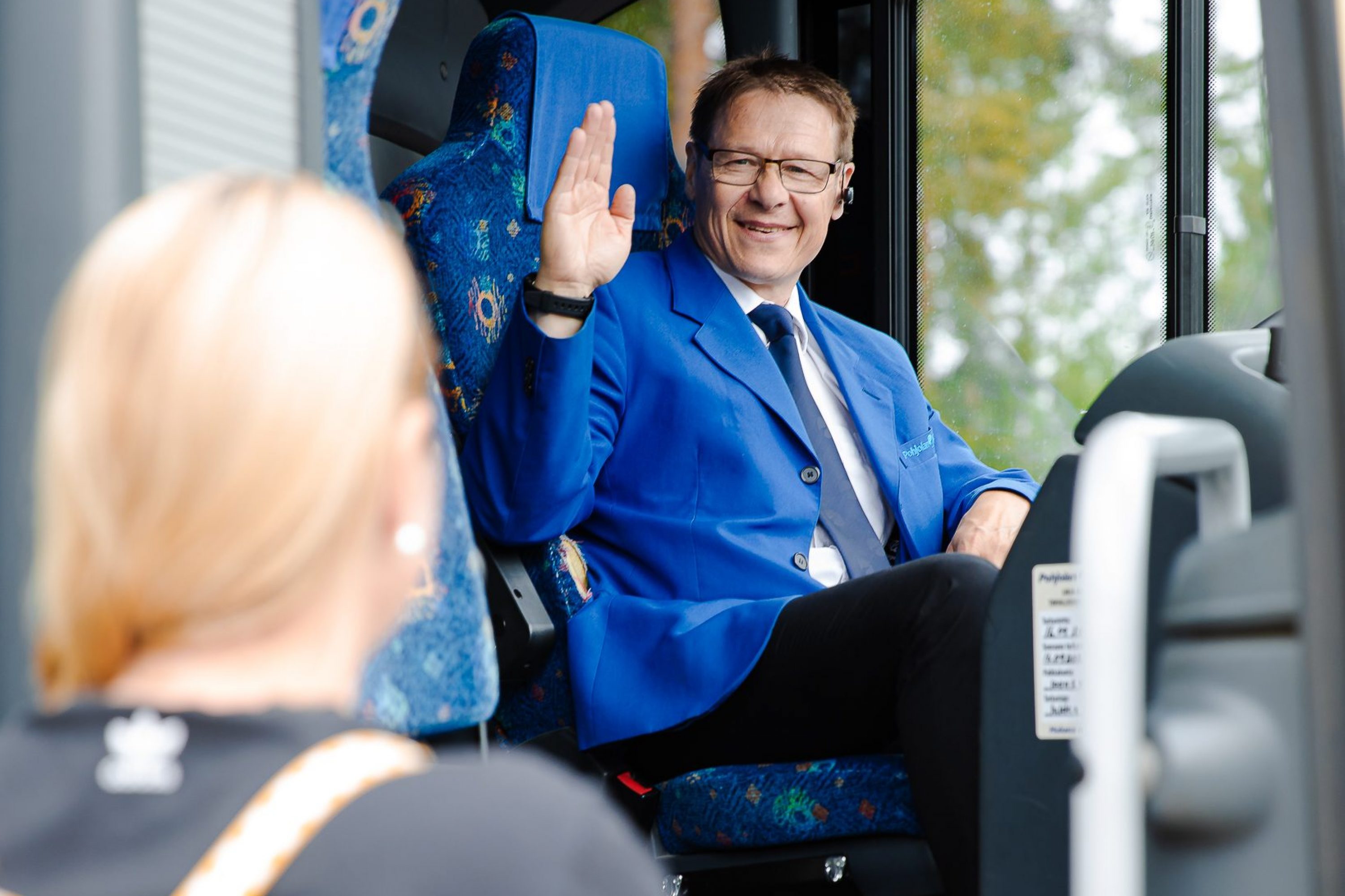 Iloinen bussinkuljettaja tervehtii matkustajaa