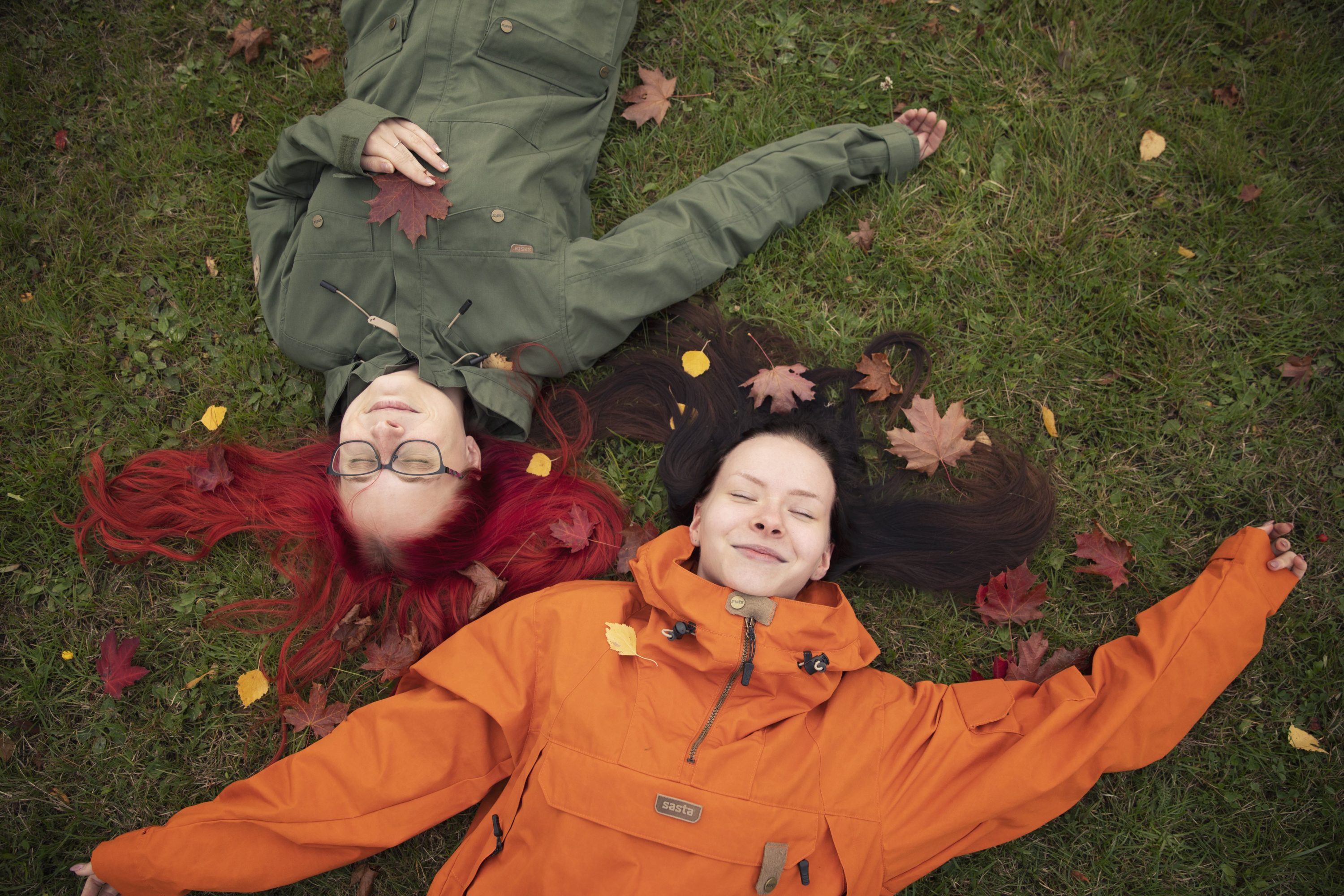 Kaksi naista makaa selällään nurmella syksyisiä lehtiä ympärillään