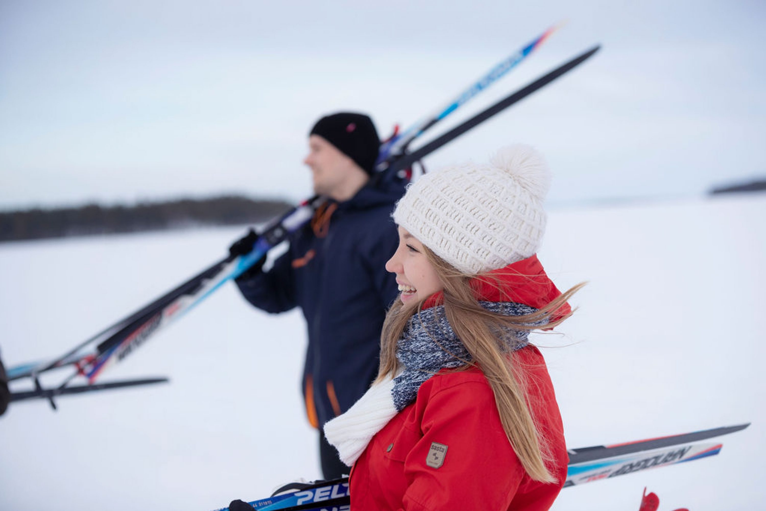 Nainen ja mies kantavat suksia järven jäällä