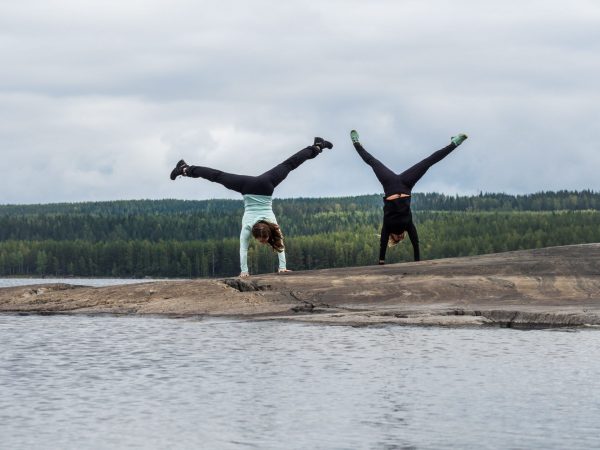 Naiset seisovat käsillään rantakalliolla