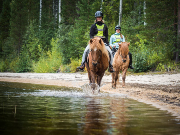 Kaksi naista ratsastamassa järven rannalla