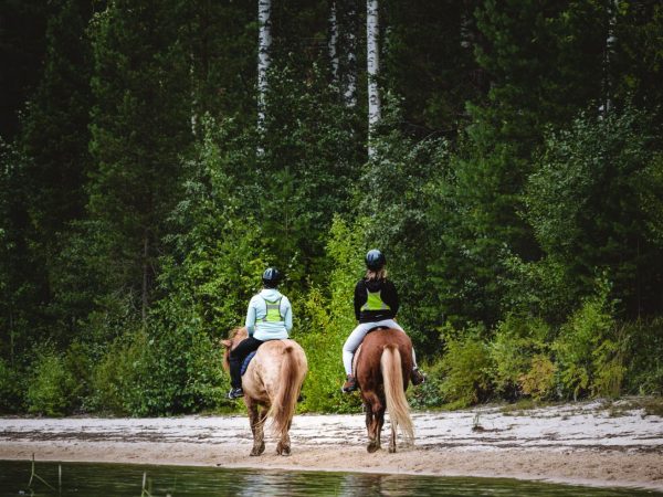 Kaksi naista ratsastamassa järven rannalla